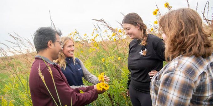 Instructors and students examining flowers in a field