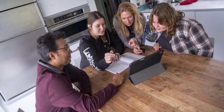 Teacher assisting students on a laptop at a desk